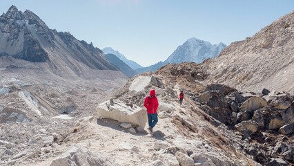 two people walking up a narrow dirt path between mountains with rocks