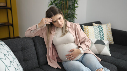 Young pregnant woman touching belly with worried expression at home