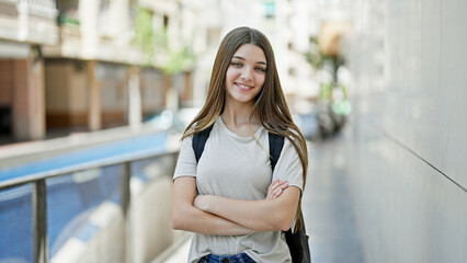 Young beautiful girl student wearing backpack standing with arms crossed gesture smiling at school