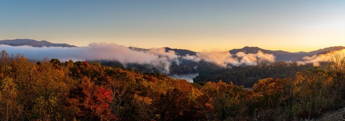 Scenic panoramic landscape featuring mountains cloaked in a mystical fog, with lush autumnal forest