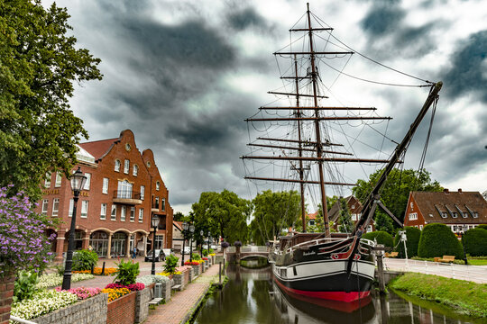 Altes Segelschiff auf dem Hauptkanal in Papenburg. Im Hintergrund ein rotes Backsteinhaus die ganz typisch f&uuml;r Papenburgs Innenstadt sind.  B&auml;ume sind ebenfalls im Hintergrund zusehen.