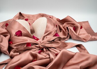 Pink satin robe and a bra with rose petals on a white surface