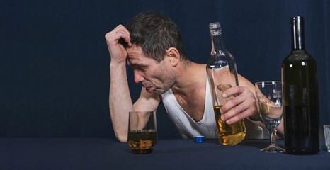 Drunken lonely man sits at table and holds his head with his hand. He feels bad. In other hand is bo