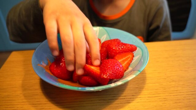 Closeup of a kid eating sliced strawberries from plate