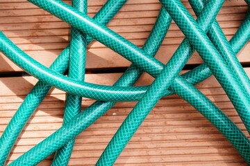 Group of interconnected green garden hoses laid on a wooden floor