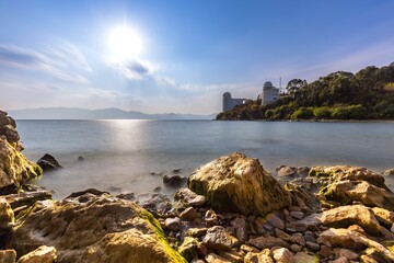 Fototapeta na wymiar Beautiful tranquil body of water surrounded by rocky shoreline, with a bright sun shining over it