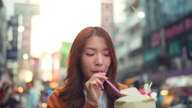 Happy young tourist Asian woman enjoy and drinking coconut juice traditional asian street food at Bangkok Chinatown, Female shopping and eating street food on summer holiday vacation.