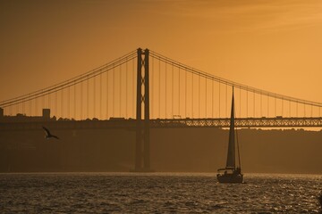 Stunning sunset view of Lisbon, Portugal, with a sailboat sailing across a bridge