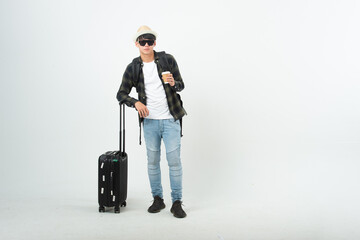 Happy asian man holding passport and tickets, ready to travel, sitting near suitcase and smiling at camera over light wall. Cheerful male traveller ready for vacation, on white background