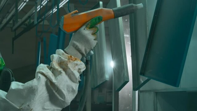 Process of powder coating of metal parts at a steel factory. Creative. Worker in protective suit with paint gun.