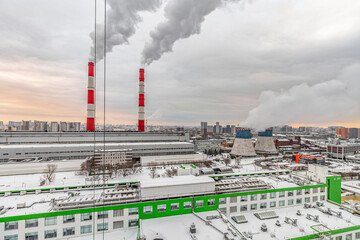 New industrial neighborhood in the capital Moscow with warehouses, heating, chimneys with smoke, high-rise apartment buildings in the daytime in winter with snow top view.