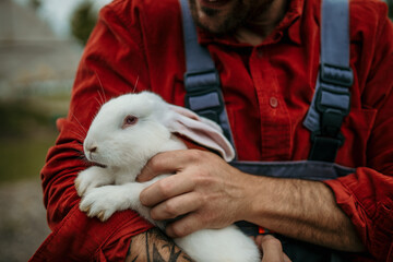 Close up image of a countryman holding a white rabbit on his farm.