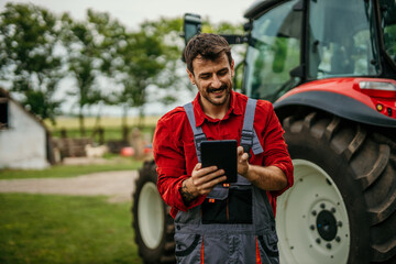 Portrait of a farmer man using a digital tablet and standing next to the tractor. Modern...