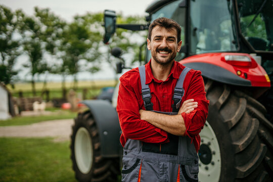 Portrait of a smiling engineer in a working suit standing in front of agricultural machinery.