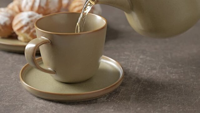 Footage of pouring tea in a cup and round eclairs on a plate.