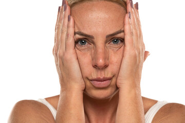 Middle aged blond woman squeezes her face skin with her hands on a white background