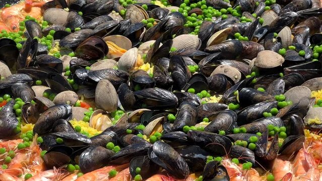4K HD video close up on clams, muscles, shrimp rice and peas cooking in a giant outdoor wok. Coastal Paella Spanish Cuisine with fresh seafood.