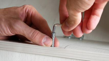 Close-up of a male hands screwing a steel bolt with a hex wrench into a wooden furniture surface