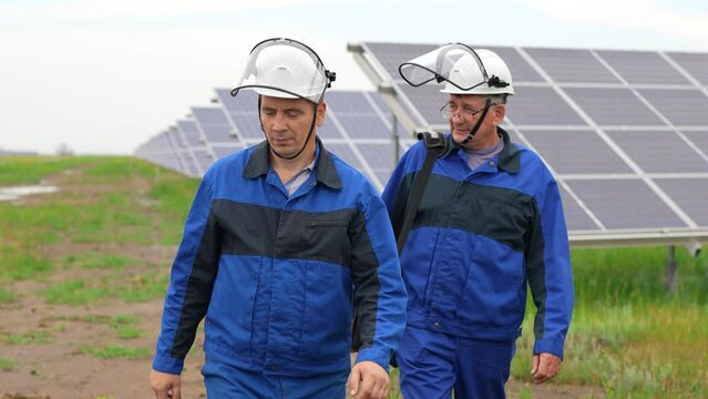 Two Service Engineers or electricians goes by solar panels, working and solving problem for green energy solar power plant operation. Technician maintenance solar cells on Solar Energy Plant