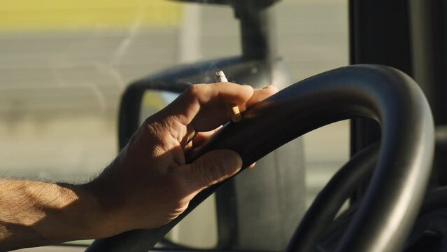 The truck driver holds a smoldering cigarette in his hands and controls the steering wheel of the car at the same time. Close-up.