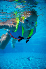 Portrait of little girl swimming underwater in goggles and vest in pool. Summer vacation