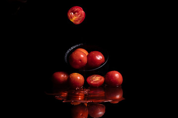 Red tomatoes in black bowl against dark background. Tomatoes reflection in water.