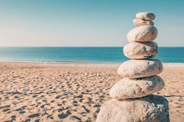 a small tower of stones as a decorative feature on a sandy beach by the turquoise sea.