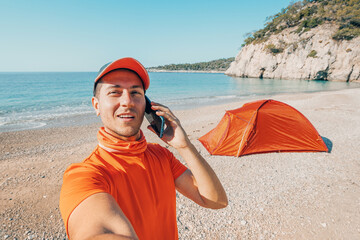 Man hiker talking by phone against his camping tent on a wild beach. Connection and communication at vacation and travel