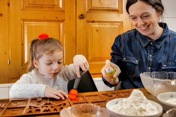 Little girl concentrated baking a gingerbread house on school holidays with the company of her...