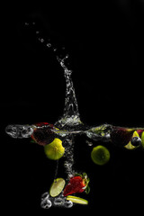 bright juicy fruits with splashes fly into the aquarium on a black background