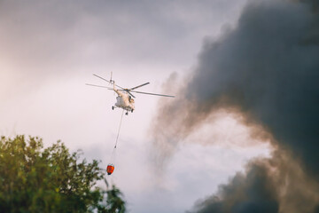 Fototapeta na wymiar a firefighter emergency helicopter extinguishes a fire and sprays water from a basket over a column of black smoke over a city or wildfire