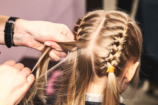 Barbershop, close up barber woman hands making braids for kid girl in hair salon. Hairdresser braided braids for pretty blonde little girl in barber shop. Hairdo, hair care concept. Copy ad text space