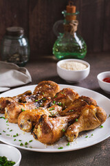 Spicy baked chicken drumsticks with green onions and sesame seeds on a plate vertical view