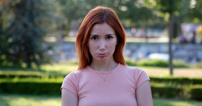 In the park, a young girl looks at the camera and, with a grumpy expression, nonchalantly shrugs her shoulders as if to say "what to me" dismissively