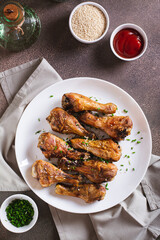 Appetizing baked chicken legs with chives and sesame seeds on a plate top and vertical view