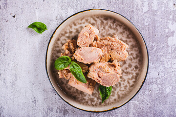 Close up of pieces of canned tuna and basil leaves on a plate top view