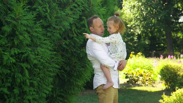 Dad holding little daughter in arms in park. Parenthood concept with copy space. Father has fun time with his daughter and keeping her in his hands. 4K, UHD