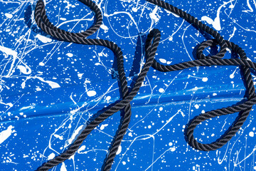 background: black rope  lying flat on a blue surface with 
 random white paint 