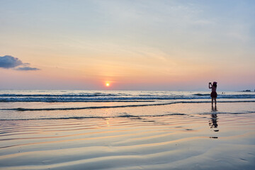 woman taking a picture of the sunset on the beach thailand
