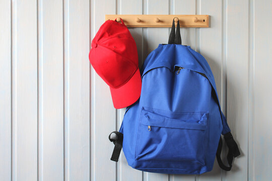 blue backpack and a red baseball cap hang on a wooden hanger.
