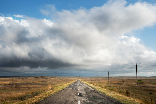 View of an old abandoned road in the steppe beautiful landscape with clouds. Freedom and travel.