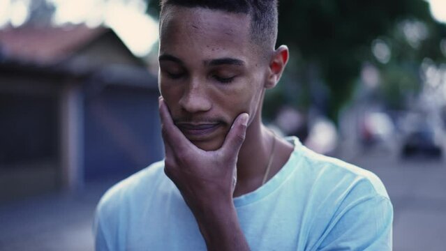 One pensive black man walking forward in street in deep mental reflection and worried emotion. Tracking motion shot of a Brazilian person strolling in urban setting