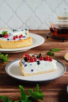 Dessert, sliced round cheesecake with blackcurrant on shortcrust pastry on a ceramic plate on a wooden background. Summer desserts, pastries with berries. Recipes dairy products.