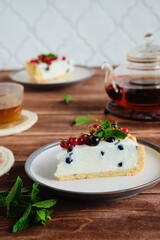 Dessert, sliced round cheesecake with blackcurrant on shortcrust pastry on a ceramic plate on a wooden background. Summer desserts, pastries with berries. Recipes dairy products.