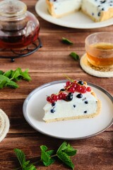 Dessert, sliced round cheesecake with blackcurrant on shortcrust pastry on a ceramic plate on a wooden background. Summer desserts, pastries with berries. Recipes dairy products.