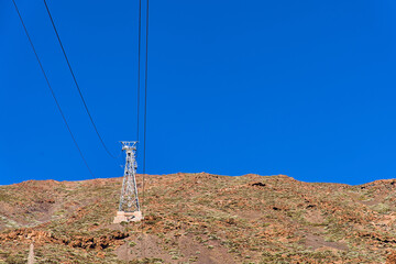 The tower of the cable car on the background of the volcano and the blue sky