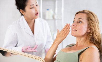 Obraz na płótnie Canvas Blonde european women listening to professional medicine worker about facial beauty procedure