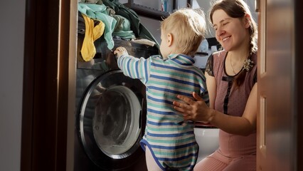 Fototapeta na wymiar Little baby boy helping mother doing laundry in washing machine. Doing housework and chores, children education and development.