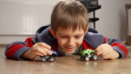 Portrait of cute smiling boy lying on floor and playing with toy cars