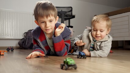 Two boys lying on wooden floor and having toy car race. Children playing, development and...